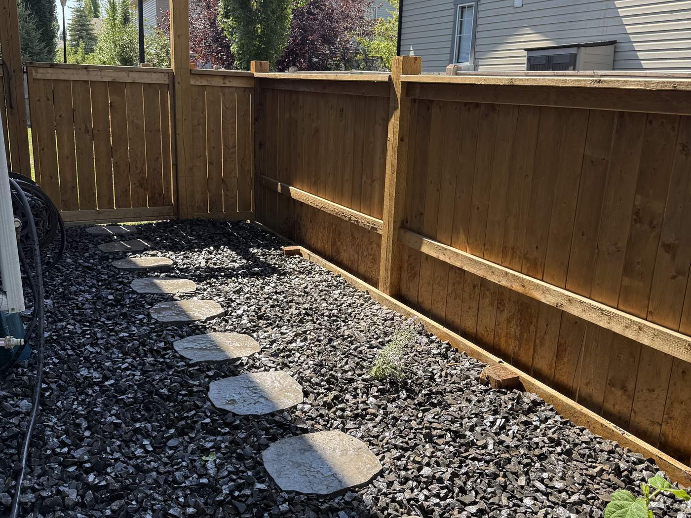 Side yard of black-and-grey Rundle rock with a line of natural stone stepping stones along a cedar fence