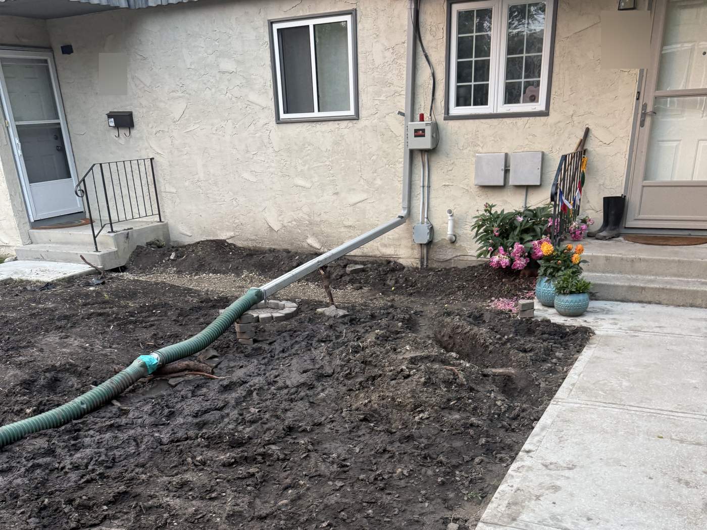 The lawn along the building at a 10-unit complex in Killarney, regraded to bare soil, a downspout hose across it