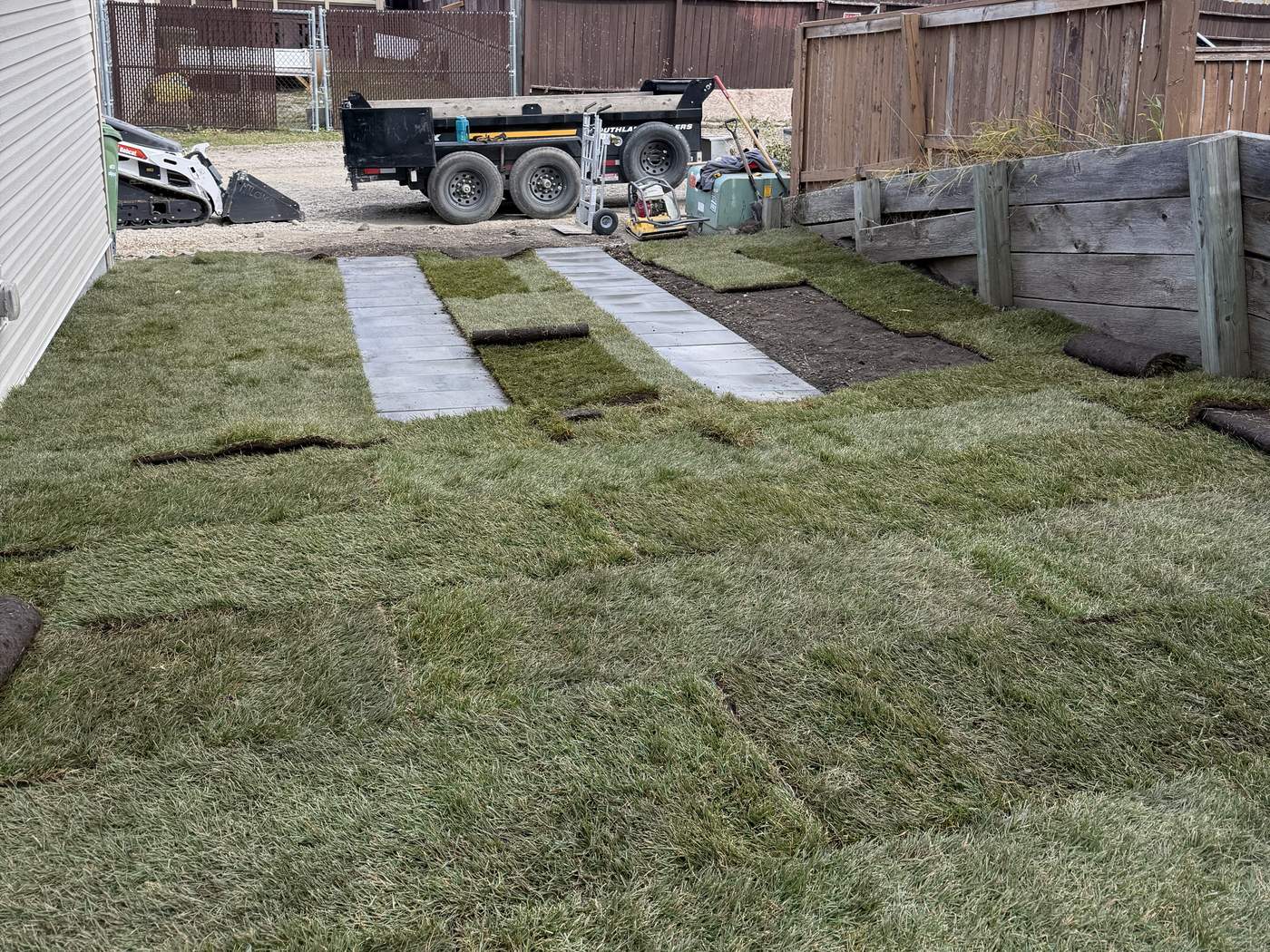 New sod being laid around two paver tire strips, with our Bobcat and dump trailer in the lane behind