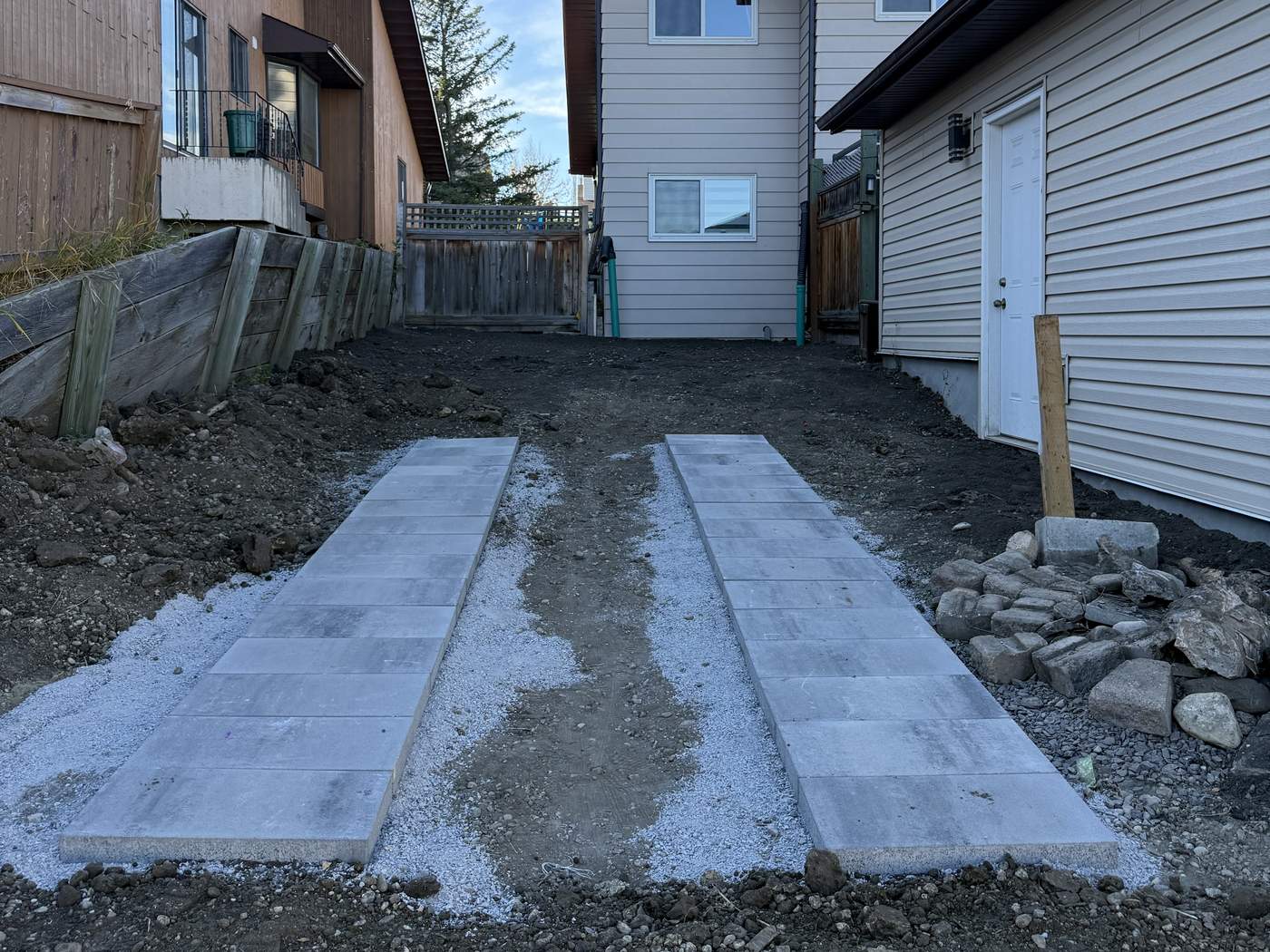 Two rows of pavers for vehicle tires set on a compacted gravel base, bare soil around them before sod