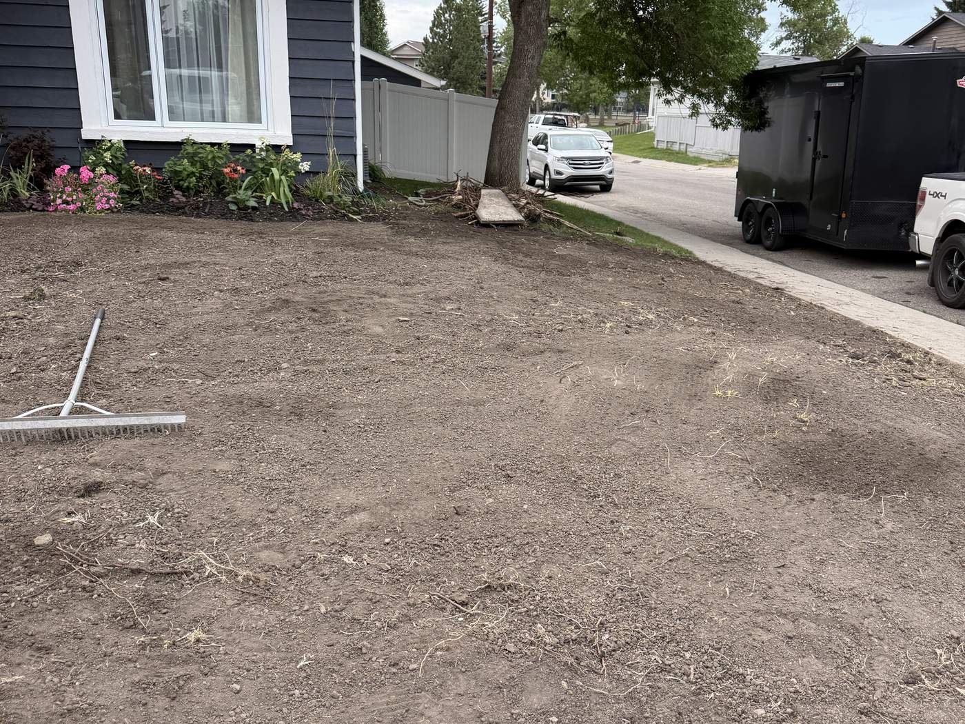 Sundance front yard with the old lawn and roots removed, graded and raked bare, a rake on the ground and flower beds by the house