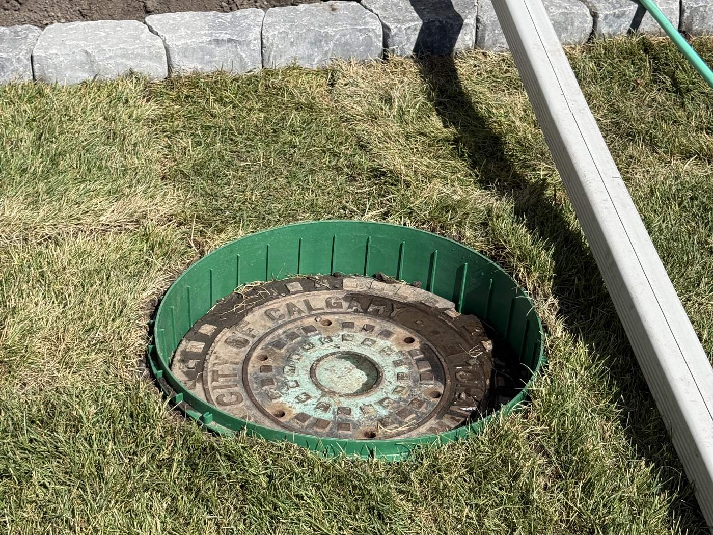 A green 6-inch riser around a lift-station lid, set flush in the new sod