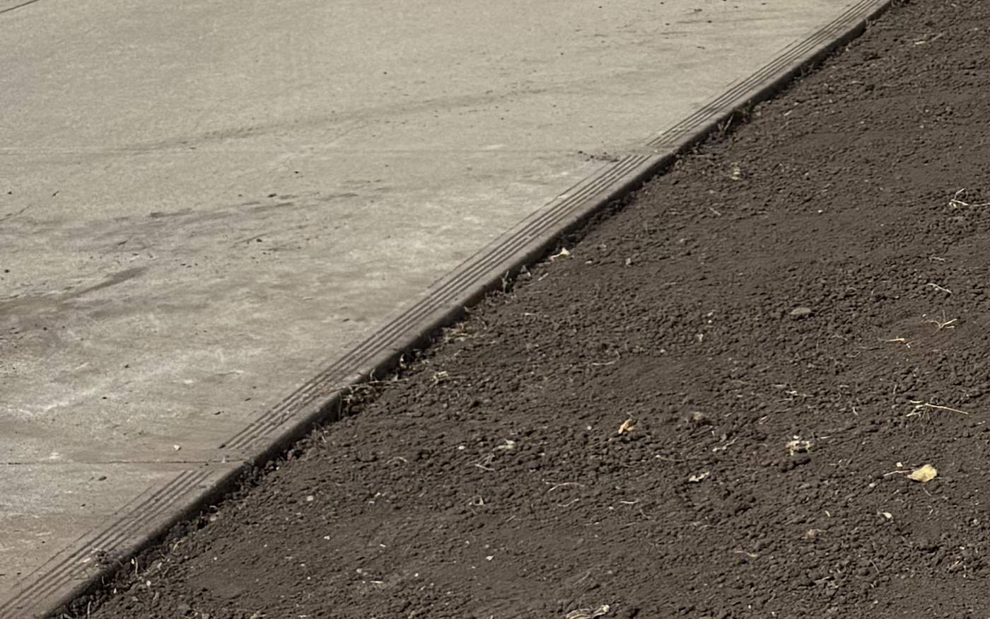 Calgary front yard stripped to bare soil and graded flat along a concrete driveway, ready for sod